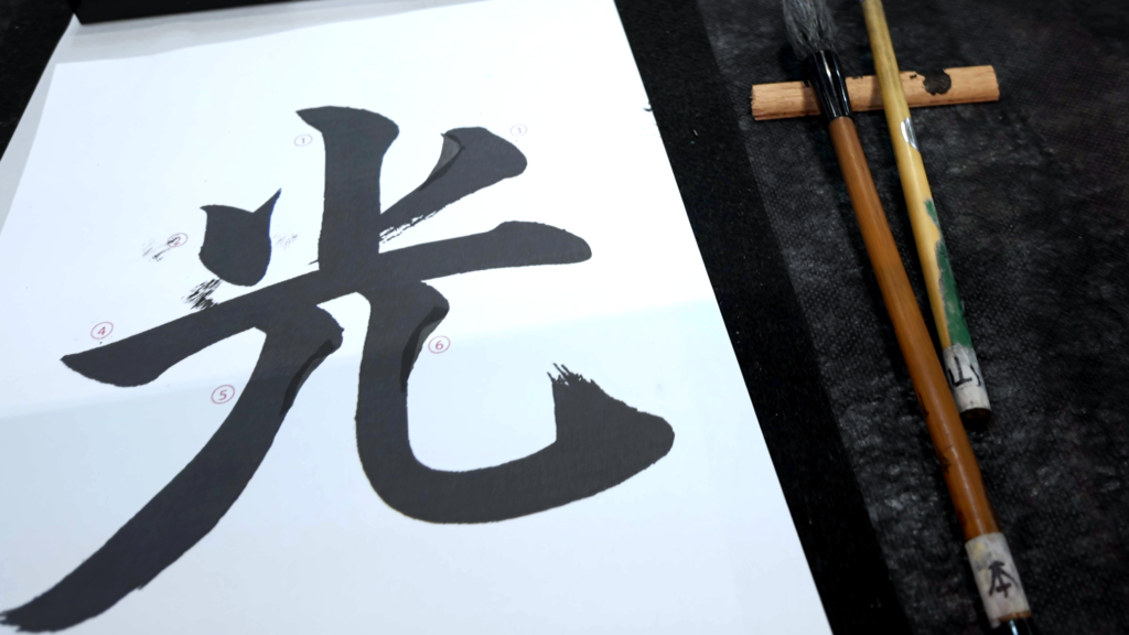 Shodo: caligrafia transformada em arte. Papel com uma letra japonesa e dois pincéis que foram utilizados